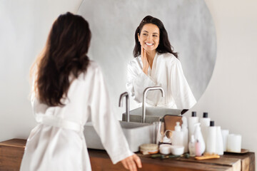 Wall Mural - Attractive brunette long-haired millennial woman looking at mirror