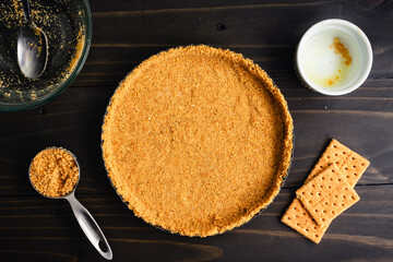 Wall Mural - Unbaked Graham Cracker Crust in a Tart Pan: Freshly made graham cracker crumb crust surrounded with kitchen tools and extra ingredients