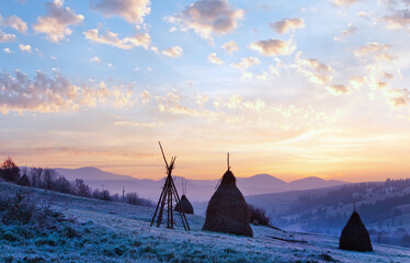 Wall Mural - first autumn frosts on pasture with haystacks and majestic sunrise in the mountains village