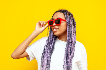 Wall Mural - young african american woman with hipster colored dreadlocks and sunglasses on yellow isolated background, girl with unique purple hairstyle looking away wearing glasses