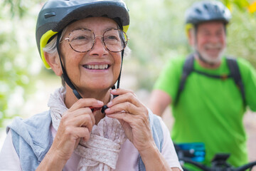 Sticker - Portrait of one old woman smiling and enjoying nature outdoors riding bike with her husband laughing. Headshot of mature female with glasses feeling healthy. Senior putting on helmet to go trip 