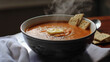 A bowl of thick, steaming homemade tomato soup with a pat of butter and crackers.