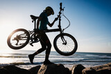 Fototapeta  - Woman taking a folding bike on sunrise seaside