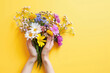 A spring bouquet in the hands of a woman on a yellow background