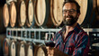 A male winemaker with a glass of wine in his hand and barrels of wine behind him