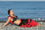 Fototapeta Perspektywa 3d - beautiful dancer woman in black and red suit lays by seashore