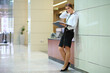 The woman with the open folder standing near the wall in the lobby of the business center