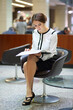 The woman with the open folder sitting on black chair in the lobby of the business center
