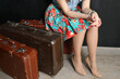 A woman in floral skirt and high heels sitting on old suitcases