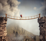 Fototapeta  - Hiker walking on a suspension bridge between mountains.