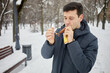 Man puffs at cigar in winter snowy park.
