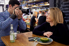 Photographer Takes Picture Of Woman Sitting At Table In Cafe.