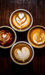 Four ceramic white coffee cups with different latte art designs on a wooden table.