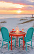Two wicker chairs and a table with a romantic dinner setting on the beach at sunset.