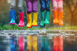 Children in colorful rubber boots playing and jumping in water puddle on a rainy day