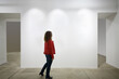Woman in red looks at white wall in exhibition of art, back view