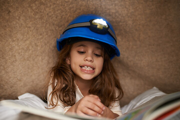 Sticker - Girl, child and book with headlamp for reading, above and learning with smile for education in family home. Kid, story and happy with light for info, language and literacy skills on floor in house