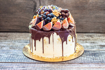 Wall Mural - Beautiful cake with figs dipped into melted chocolate, pecan nuts, grapes, chocolate bites and cookies on the top on rustic background