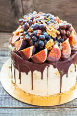 Wall Mural - Beautiful cake with figs dipped into melted chocolate, pecan nuts, grapes, chocolate bites and cookies on the top on rustic background
