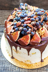 Wall Mural - Beautiful cake with figs dipped into melted chocolate, pecan nuts, grapes, chocolate bites and cookies on the top on rustic background