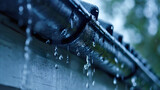 Fototapeta  - Closeup of the rain falling on the aluminum gutter on the house shingles roof, water drainage