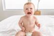 © Louis-Paul Photo - Baby boy in diaper on white sunny bedroom. one years child relaxing in bed.