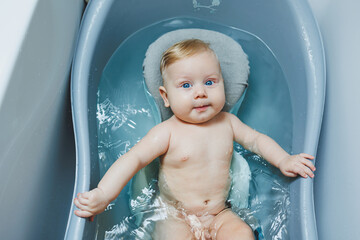 Wall Mural - Hygiene of newborns and children. The baby lies on a stand and bathes in a bathtub. Bathing a newborn baby in a bath