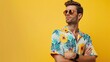 Portrait of a young man with a beard and sunglasses, wears a colorful Hawaiian t-shirt, isolated on yellow background.