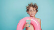 Shirtless young boy with inflatable ring and glass of cocktail on pastel blue background