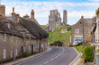 Corfe Castle ruins in Dorset on a sunny summer’s day with traditional Portland stone cottages lining the road