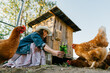 Happy middle aged woman on a private farm feeding chickens. Joyful farmer woman caring for her bird in her backyard in a rustic style, demonstrating an eco-friendly lifestyle. Sustainable lifestyle