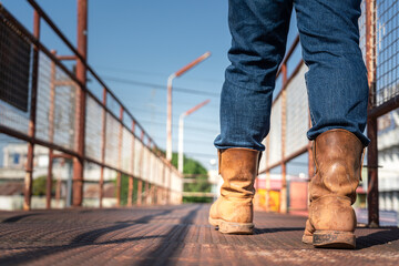 Wall Mural - Close-up at worker feet is wearing leather safety boots during walking on rustic walkway platform. Ready to working in the challenge industrial concept scene.