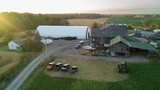 Fototapeta Uliczki - A high up aerial drone shot of a farmhouse, farm fields and Barns at sunset