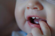 Macro shot of an infant's smile showing the first tooth, with a gentle fingertip pointing at it