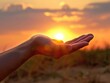 A hand extended towards a setting or rising sun, capturing the warmth of the light and creating a hopeful, peaceful feeling