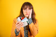 A concerned young woman holding several credit cards, hand to face, on a yellow background.