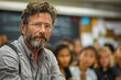 © Good Shot - Close-up of a focused male teacher with a beard and glasses in a classroom setting.