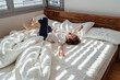 Cute little happy toddler boy lying on bed with his teddy bear toy playing and having fun at sunny morning. Light and shadows
