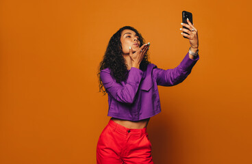 Wall Mural - Vibrant woman taking selfie against bright orange background with modern smartphone