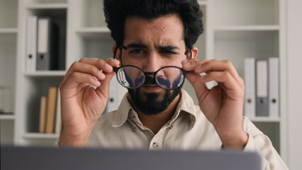 Wall Mural - Unhealthy Indian Arabian man in glasses for laptop business work confused businessman office ceo with bad eyesight blurry vision eyes myopia take off spectacles medical eye laser correction loss sight