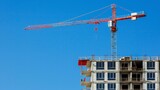 Fototapeta  - Crane and uncompleted building on construction site with blue sky background for text