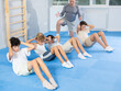 Diligent preteen trainee practicing press in lying position with other boys and teacher in sports hall