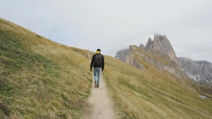 Wall Mural - Man traveler walks to the famous Mount Seceda in the Dolomites. Mountain trail in Alps mountains in autumn or winter. Beautiful alpine mountains in Italy. Seceda, one of the most beautiful mountains