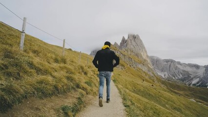 Wall Mural - Man traveler walks to the famous Mount Seceda in the Dolomites. Mountain trail in Alps mountains in autumn or winter. Beautiful alpine mountains in Italy. Seceda, one of the most beautiful mountains