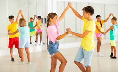 Wall Mural - Interested modern tween boy and girl practicing dynamic boogie-woogie in pair during group class in dance studio for children.