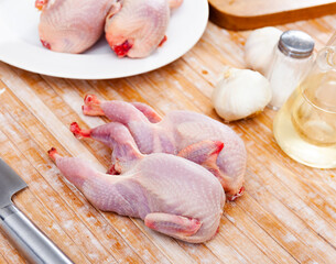 Wall Mural - Uncooked quails on on wooden table and white plate. Home kitchen, preparing food.