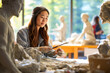 An aspiring Young Asian female sculptor shapes clay into art in art class. Students in a vibrant studio on a art workshop background. Concept of teaching applied art, sculpture. Copy space