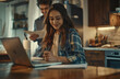 A young couple doing financial planning at home, smiling and working together on paper documents with a laptop in the kitchen. The concept of a positive attitude