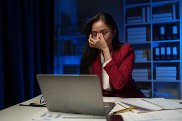 Wall Mural - Asian businesswoman is tired, headache, sleepy and bored from sitting at a desk for a long time working on a laptop computer. Problematic financial paperwork Office syndrome concept.