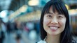 Happy young Asian woman with black hair smiling and looking at camera on blurred background of railway station in London United Kingdom : Generative AI
